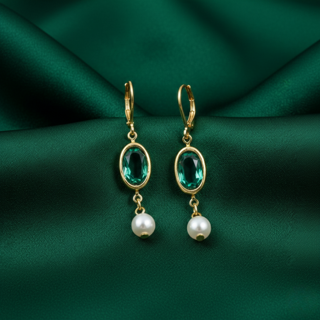 Gold earrings with green gemstones and pearl drops on a green fabric background