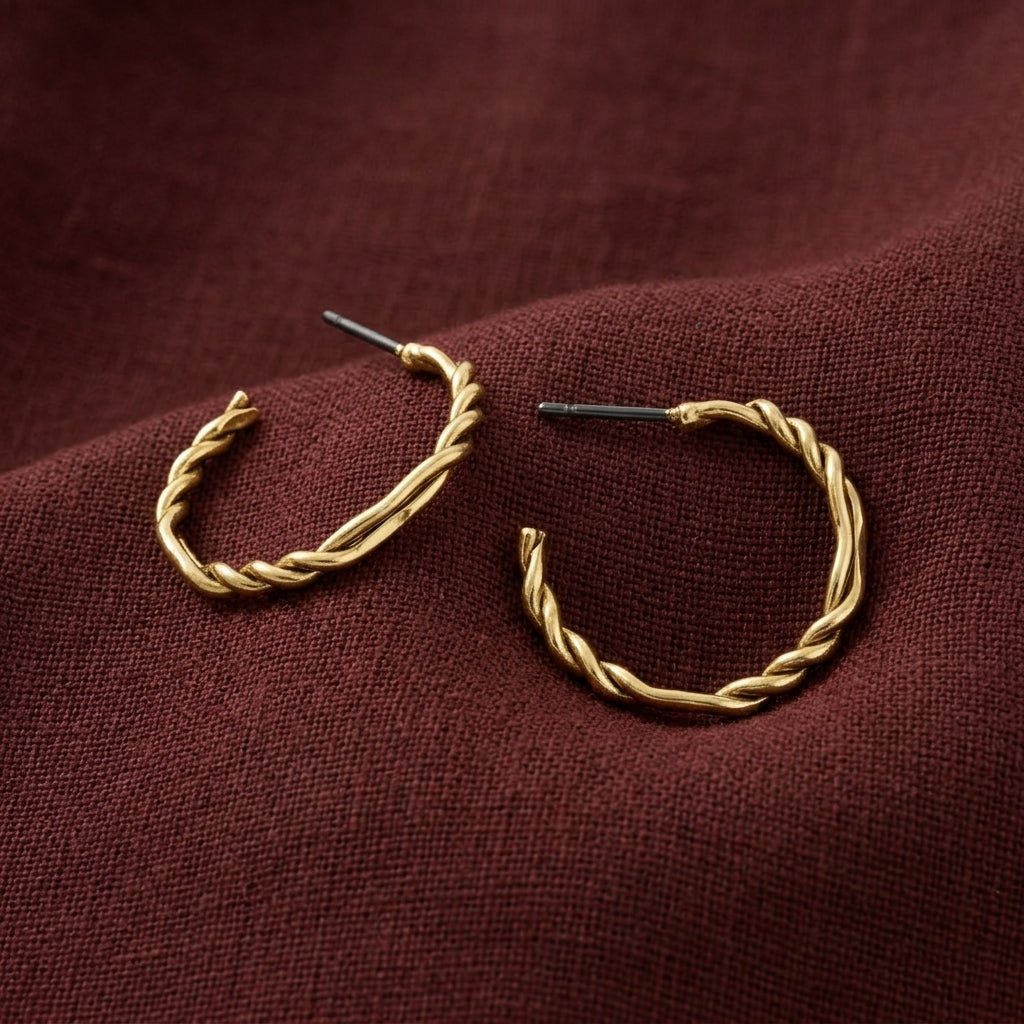 Twisted gold hoop earrings with post backs, displayed on a textured dark burgundy fabric background.