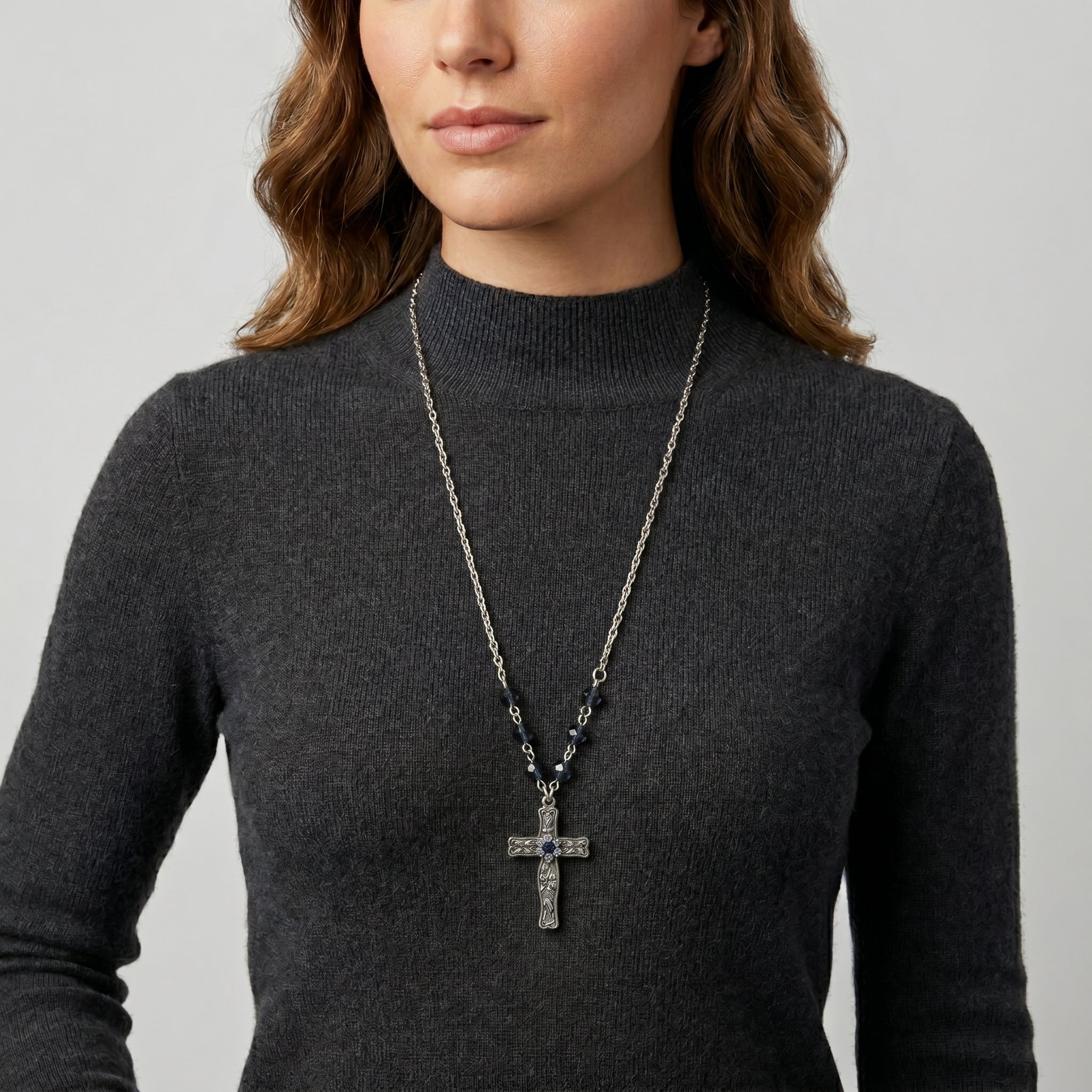 Person wearing a dark gray turtleneck sweater with a long necklace featuring a cross pendant and Montana Blue crystals.