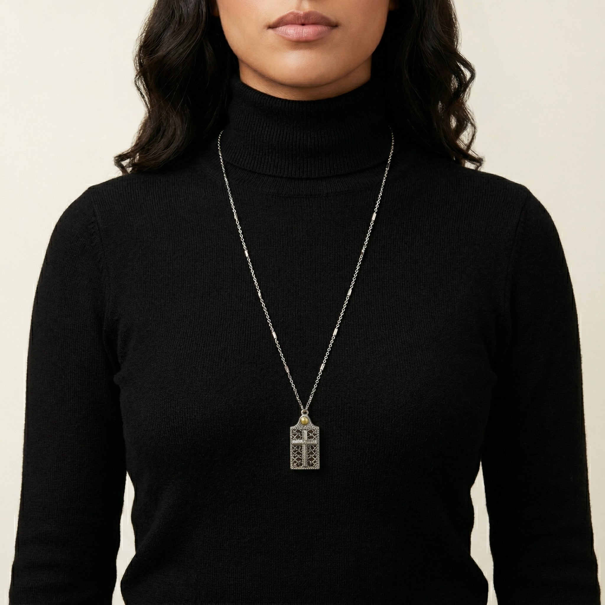 Person wearing a black turtleneck with a long cross necklace against a neutral background