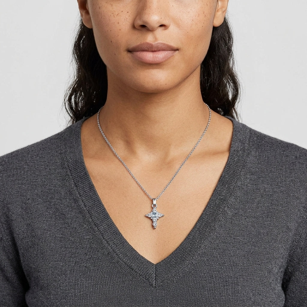 Woman wearing a silver necklace with a cross pendant and clear and blue crystals on a plain background