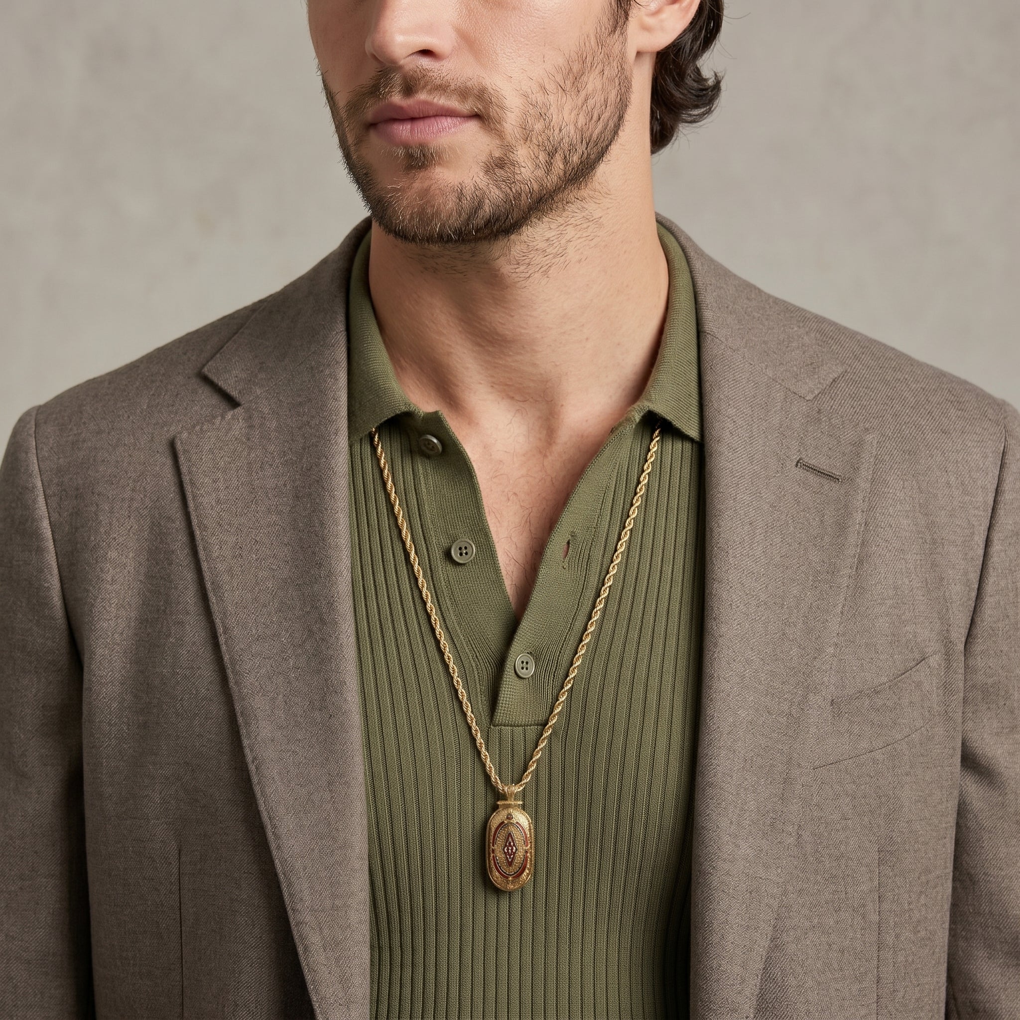 Man wearing a brown blazer and green shirt with a gold pendant necklace against a neutral background