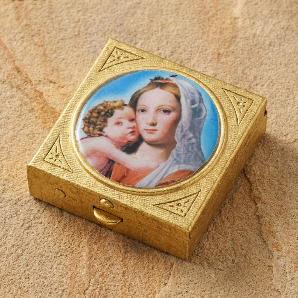 Decorative gold tone pillbox with a portrait of a Madonna and Child placed on a beige stone surface