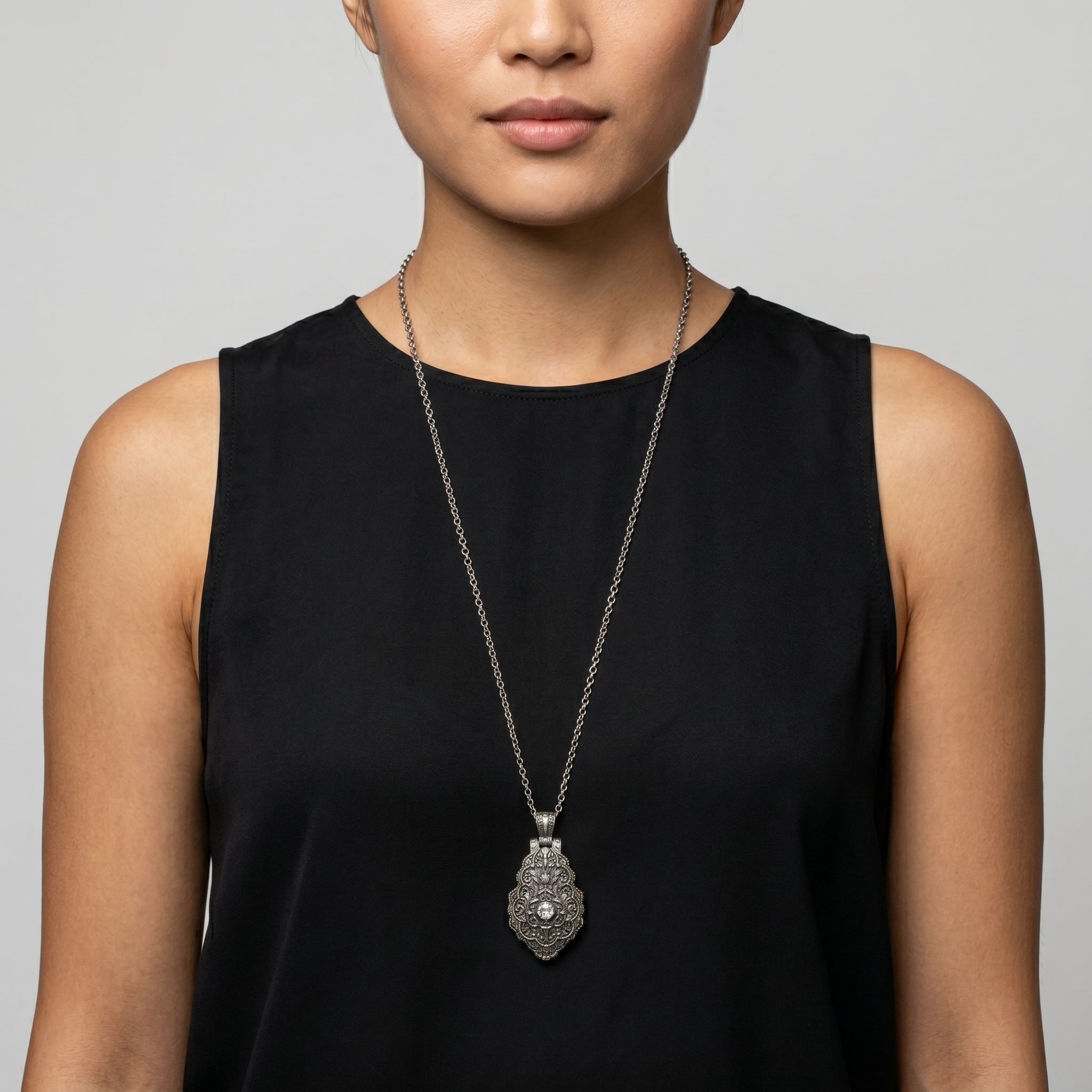 Woman wearing a black sleeveless top with a silver locket necklace against a gray background