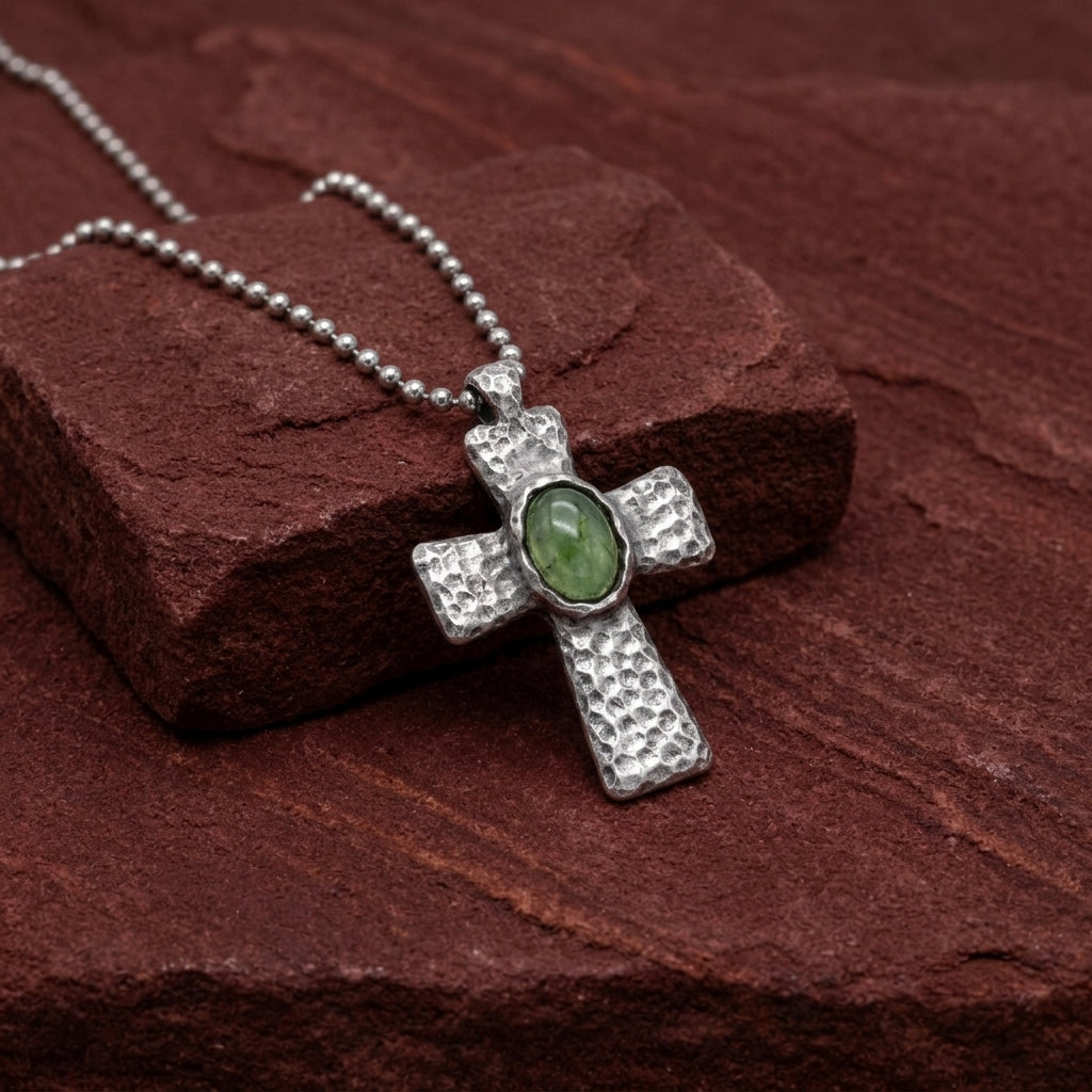 Silver cross pendant with a green gemstone on a brown stone surface