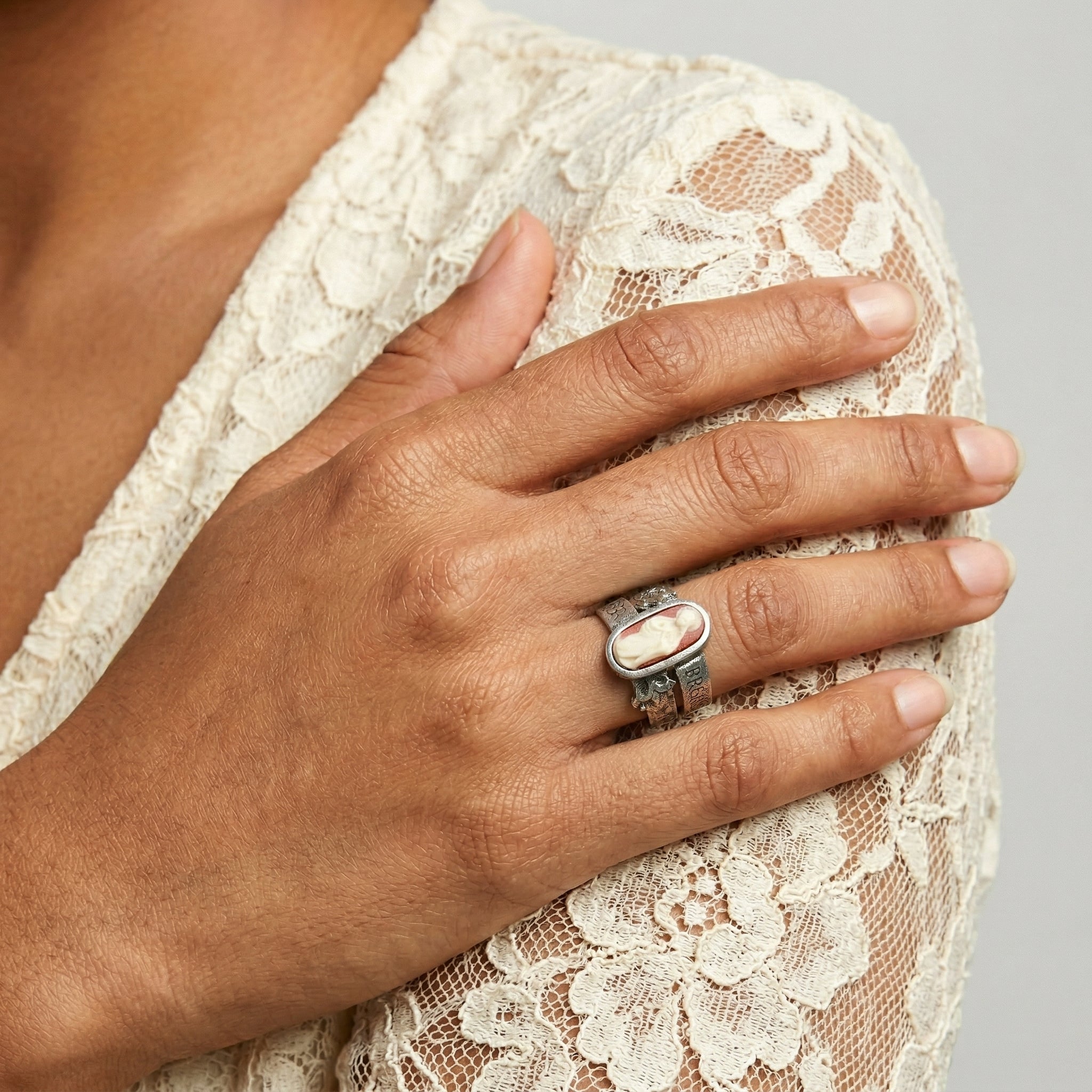 Hand wearing a silver ring with a resin red and ivory cameo resting on a lace garment.