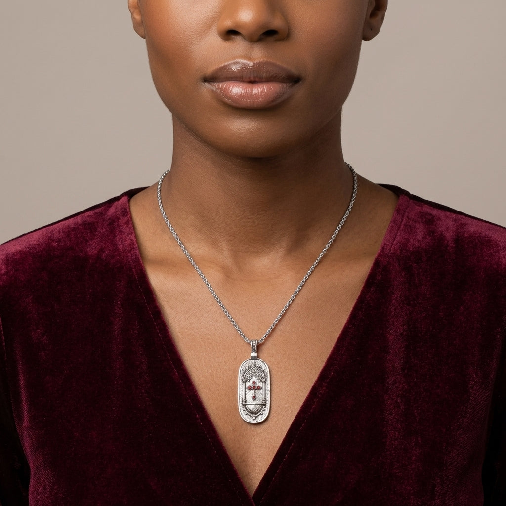 Woman wearing a silver necklace with a pendant that has a cross design against a neutral background