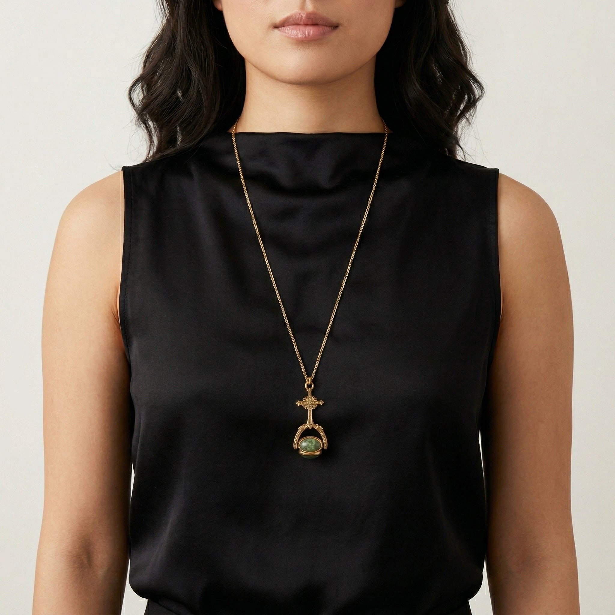 Woman wearing a black sleeveless top with a gold tone necklace featuring a cross-design spinner pendant with three different types of gemstones