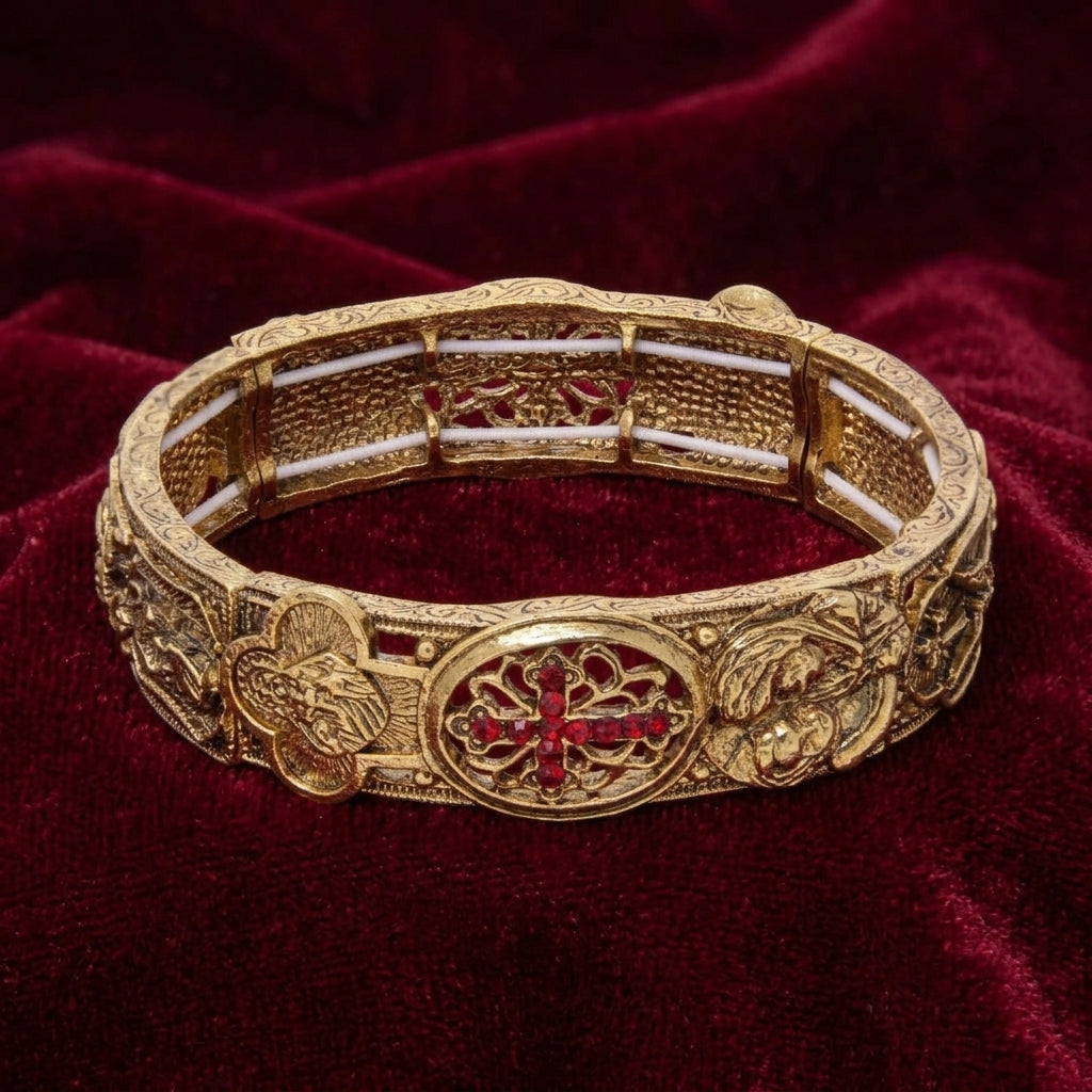 Gold bracelet with intricate religious designs and a red crystal cross on a red fabric background