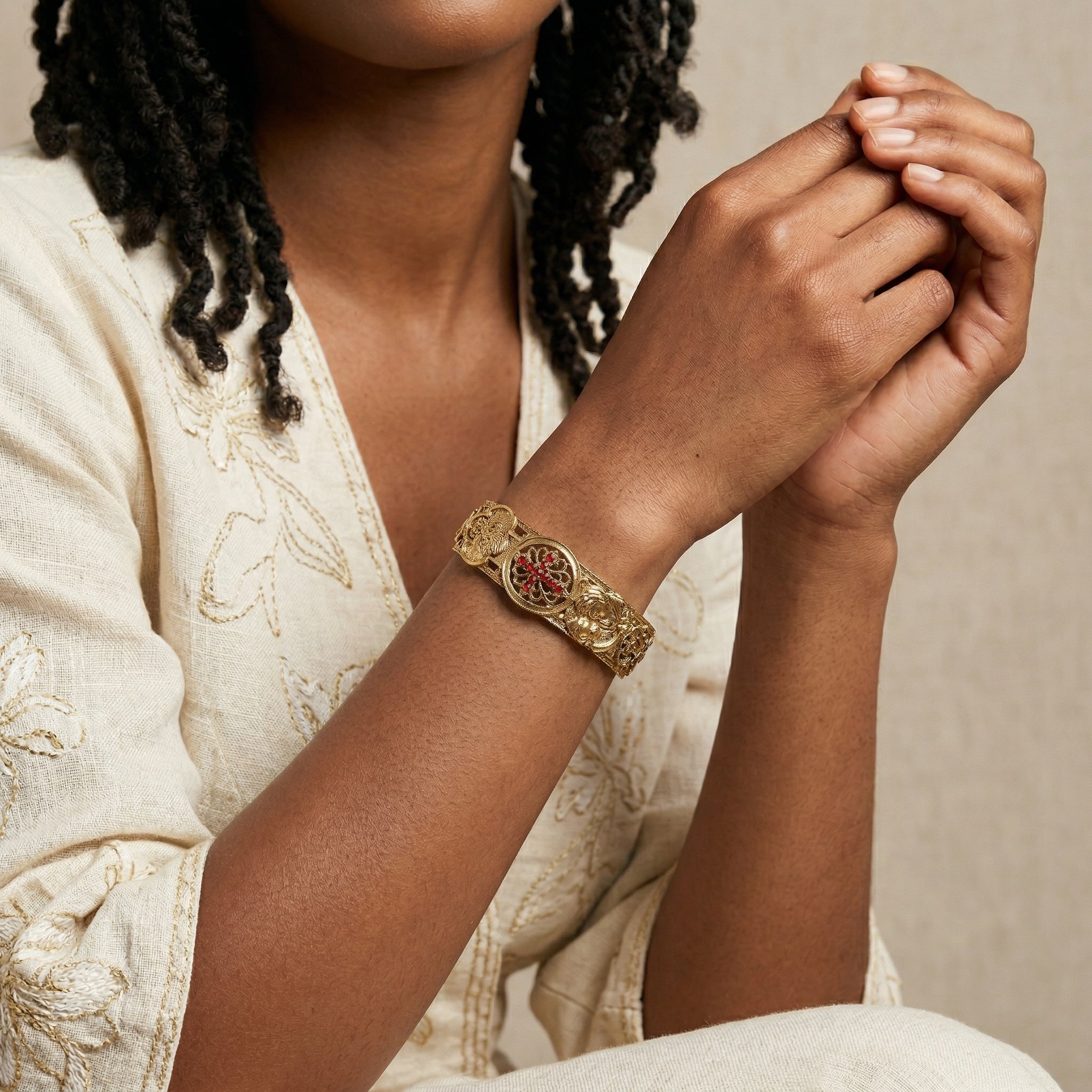 Woman wearing a gold bracelet with a red crystal cross on a beige background