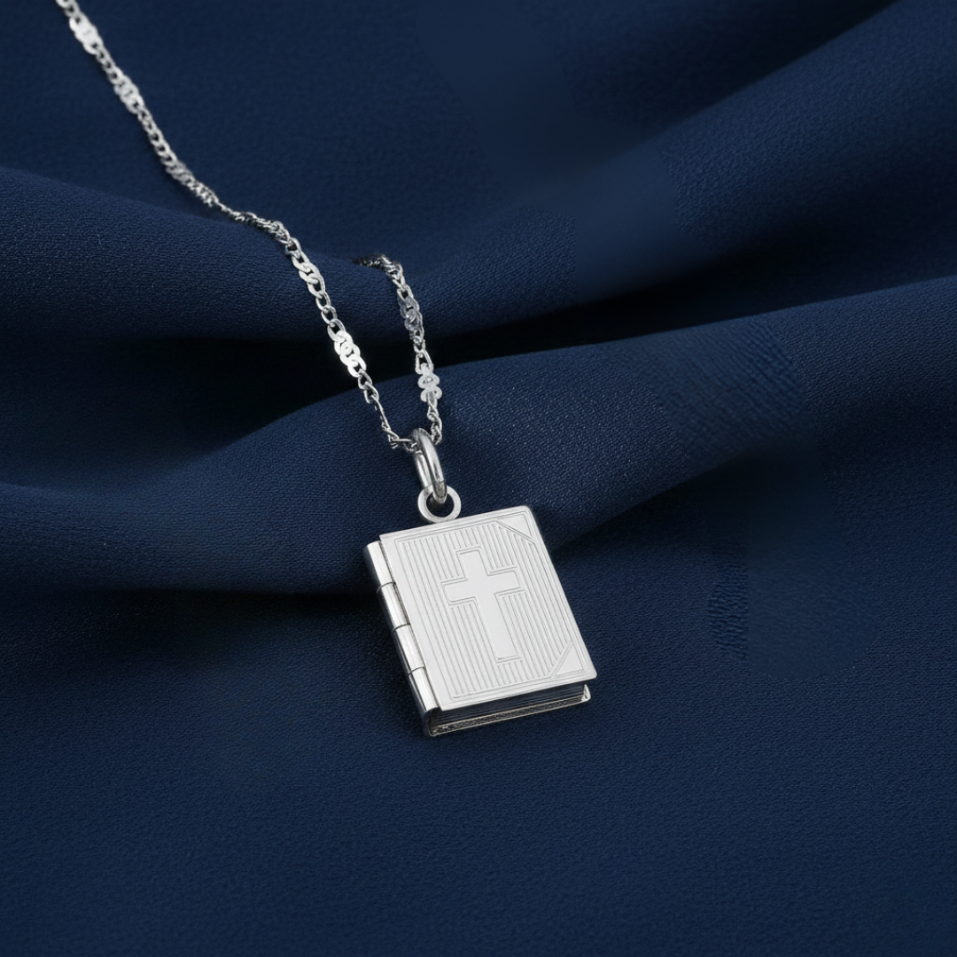 Silver necklace with a Bible-shaped pendant on a dark blue fabric background