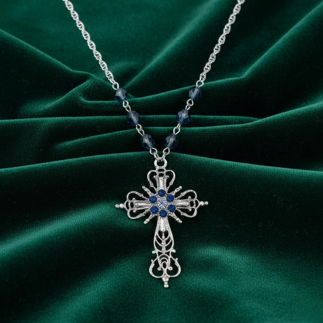 Silver cross necklace with blue stones on a green fabric background.