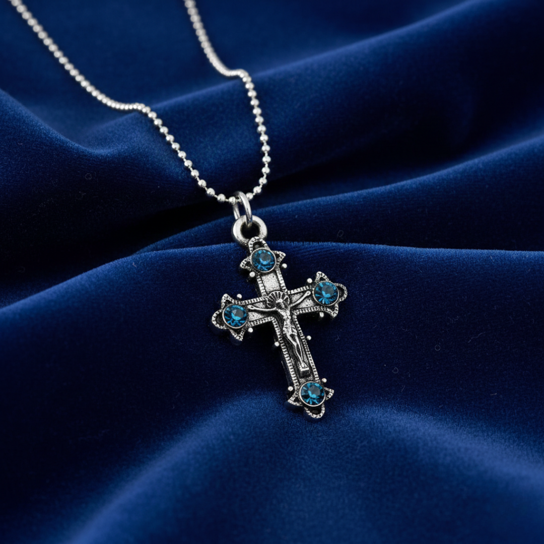 Silver cross necklace with blue stones on a blue fabric background