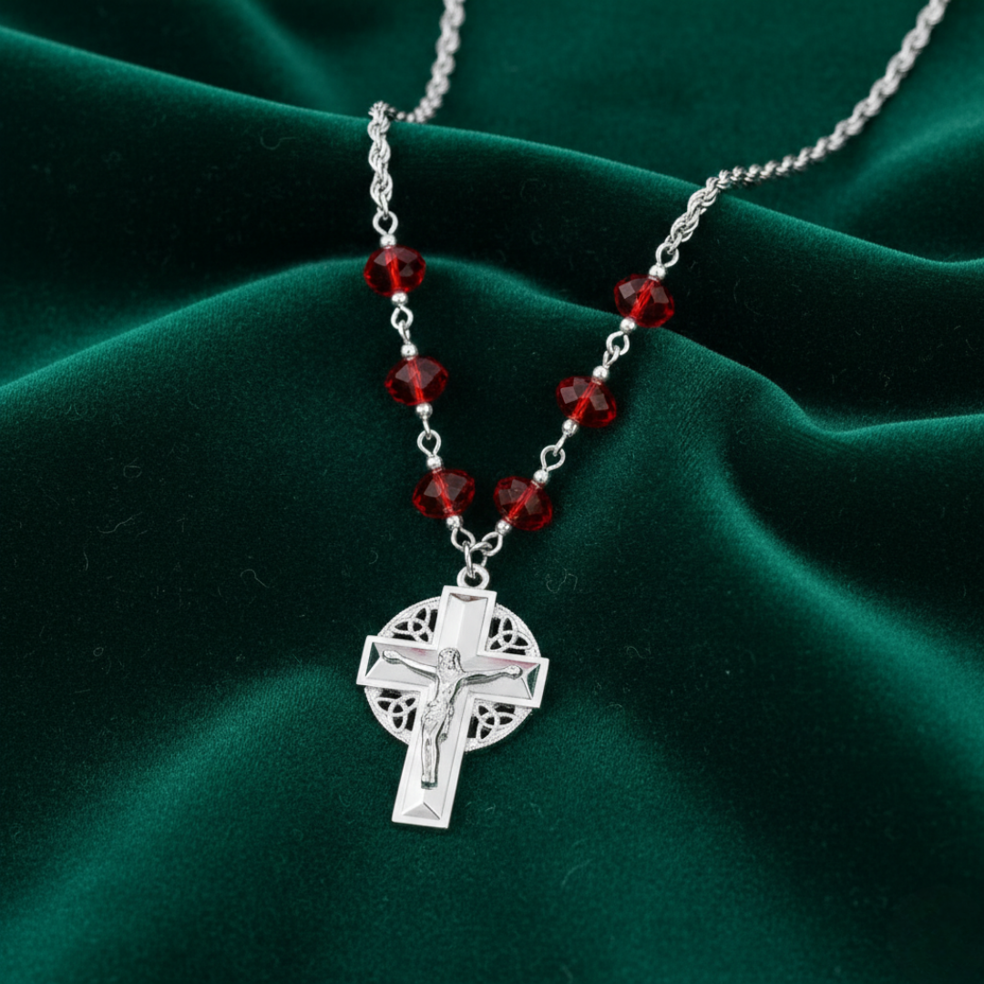 Silver cross pendant necklace with red beads on a green fabric background