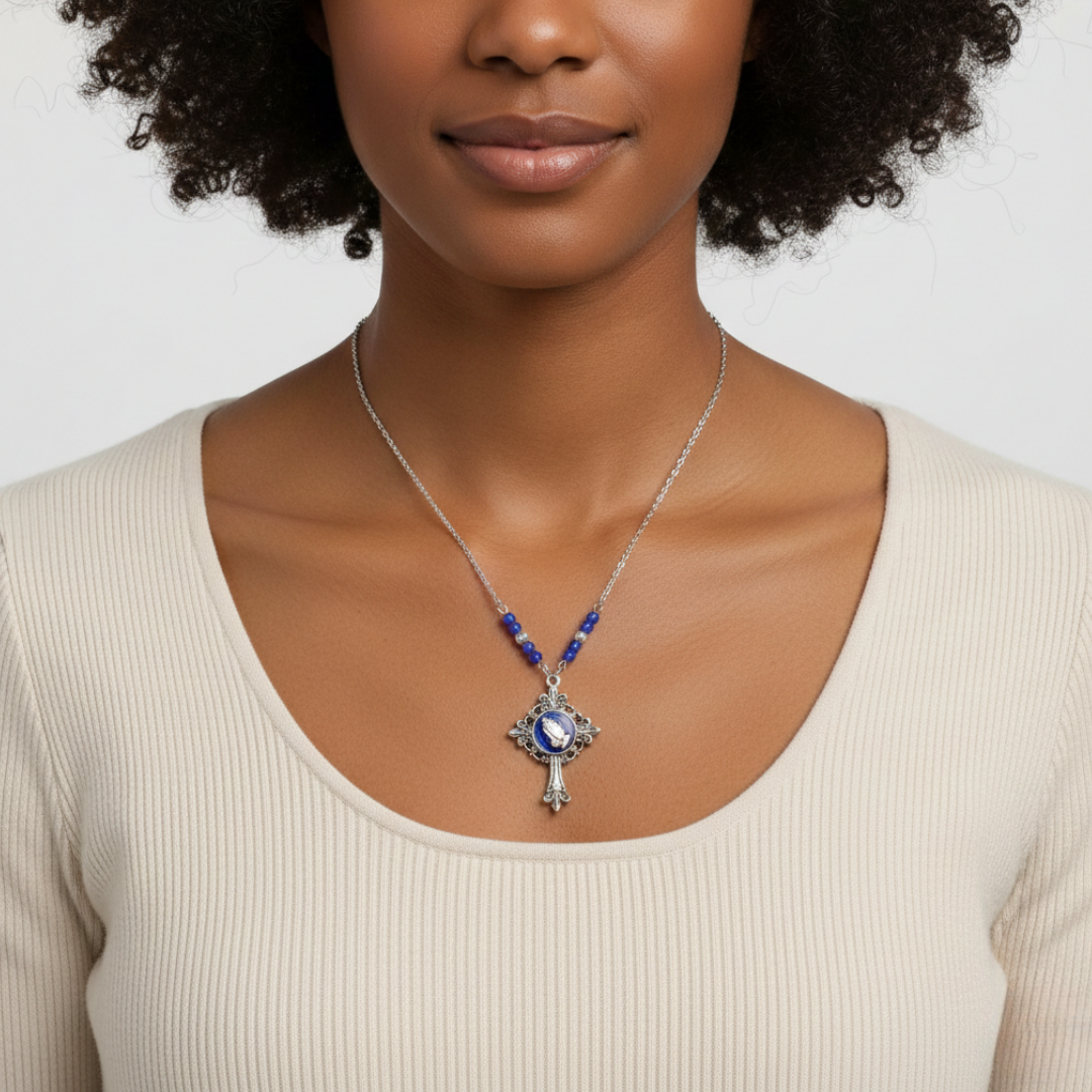 Woman wearing a silver necklace with a blue beads and a blue pendant of praying hands on a plain background.