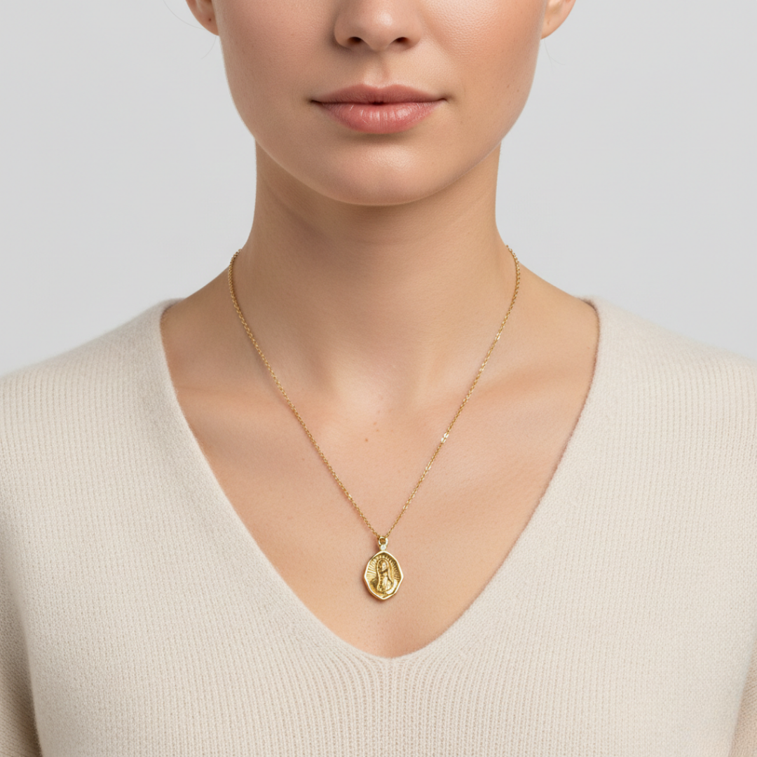 Gold necklace with a pendant of Mary praying worn by a person on a plain background