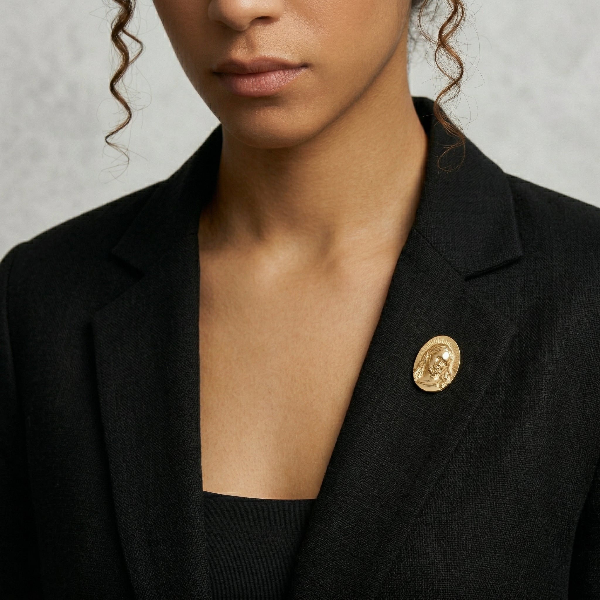 Woman in a black blazer wearing an all-Gold Jesus brooch