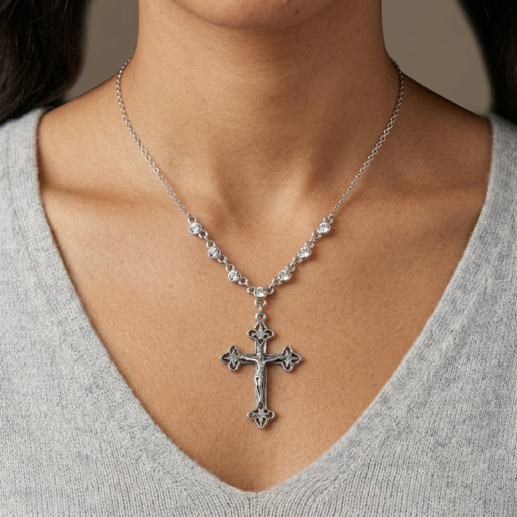 Silver necklace that has crystals on the chain with a cross pendant worn by a person in a gray sweater.