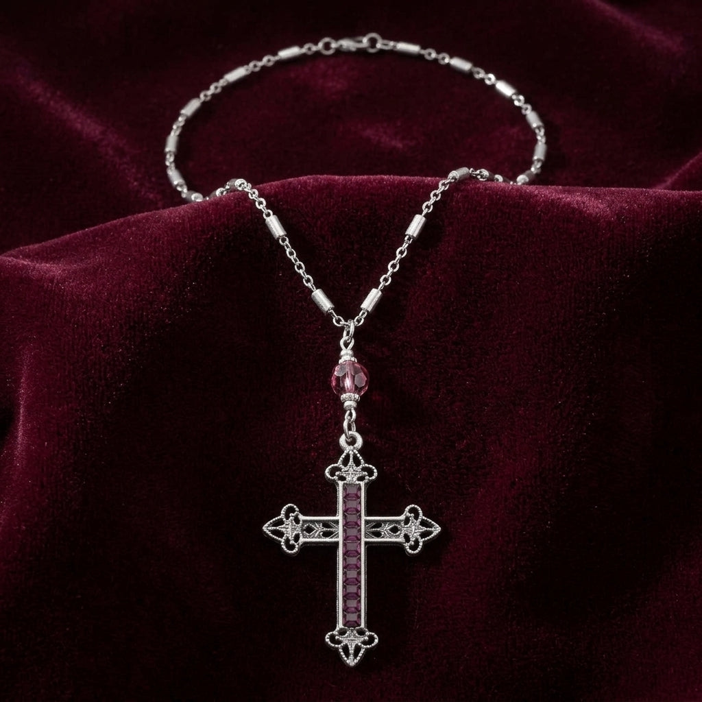 Silver tone cross pendant necklace with amethyst crystal accents resting on a burgundy colored fabric