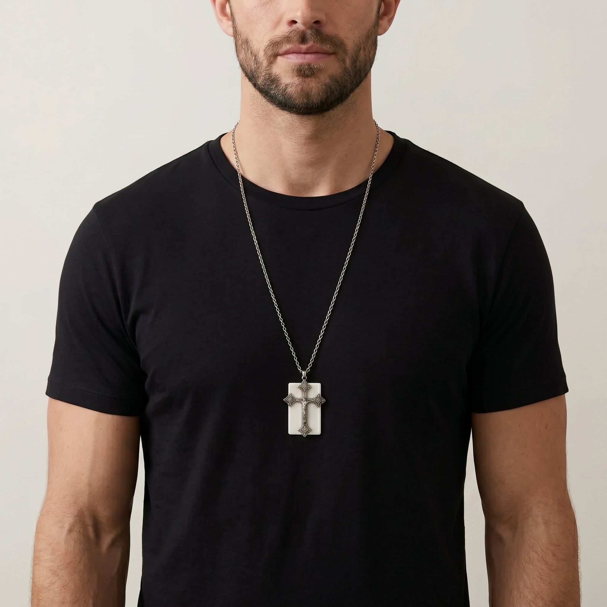 Man wearing a black t-shirt and a necklace with a cross pendant on a plain background