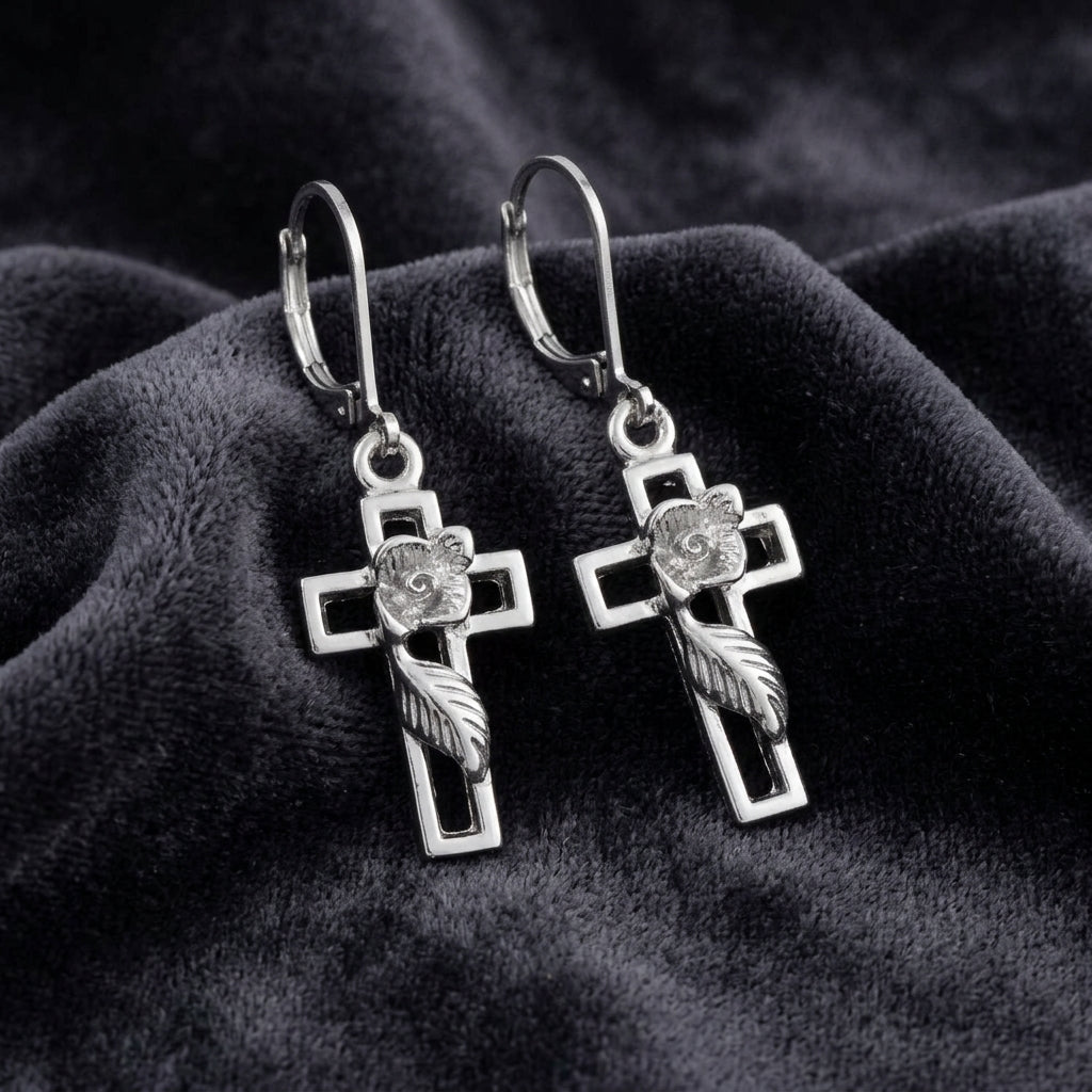 Silver cross earrings with feather designs on a dark fabric background