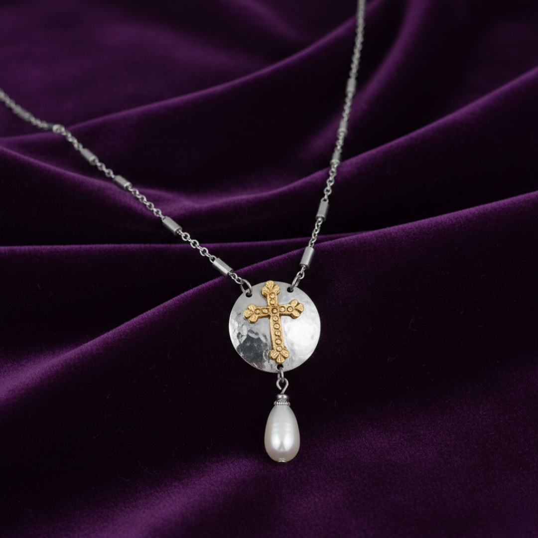 Necklace with a cross pendant and pearl drop on a purple fabric background