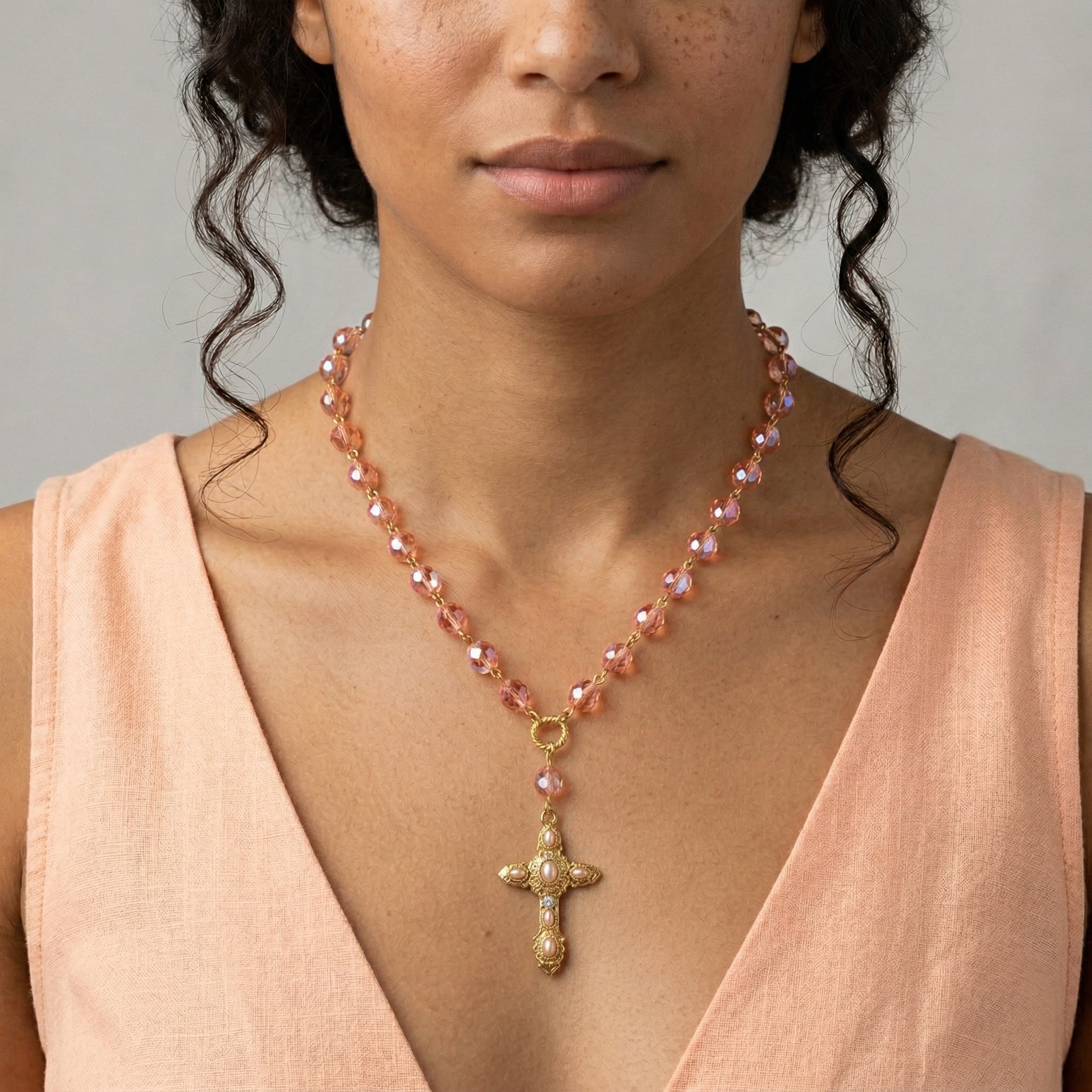 Woman wearing a pink beaded necklace with a gold cross pendant against a neutral background