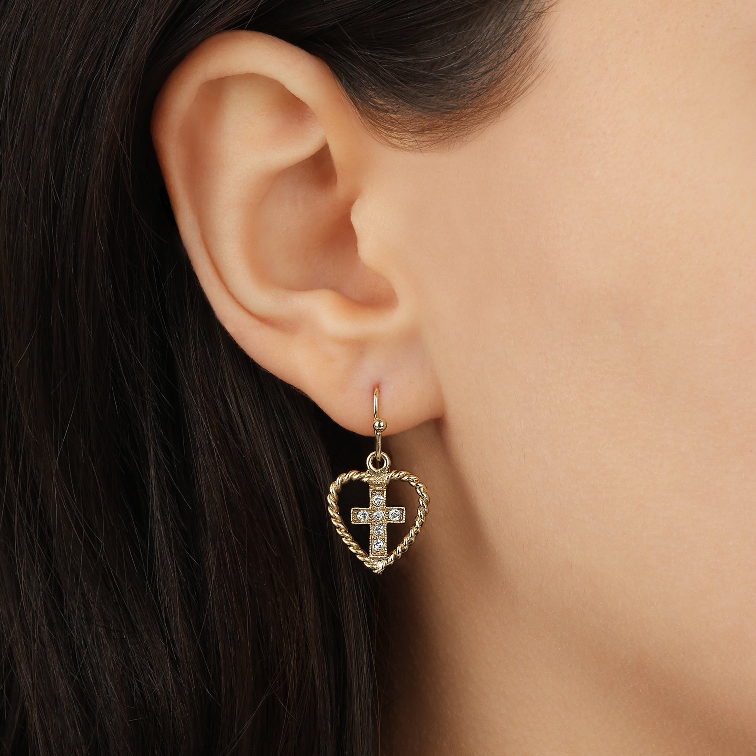 A close-up of a model's ear wearing a Golden Roped Heart & Clear Crystal Cross Drop Earrings