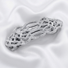 Silver barrette with intricate design on a white satin background