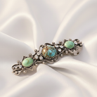 Decorative hair barrette with turquoise stones on a white satin background