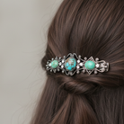 Decorative barrette with turquoise stones in a braided hairstyle on a neutral background.