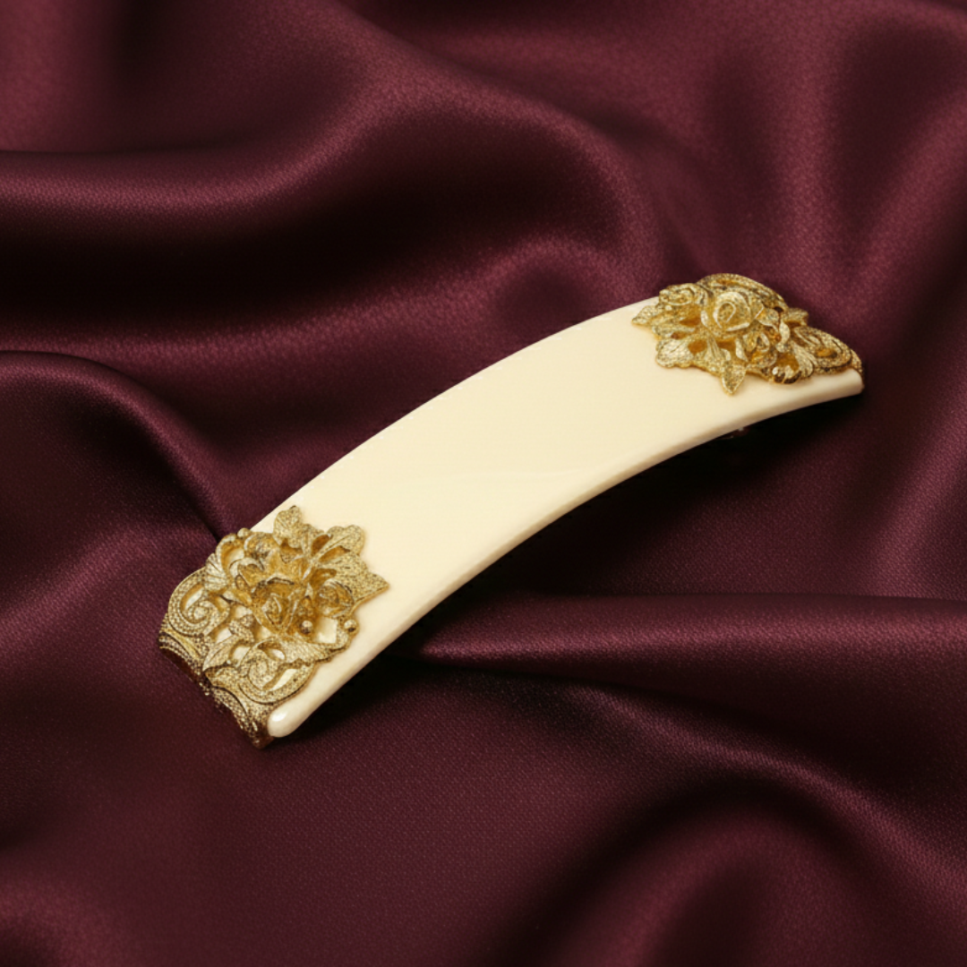 Decorative hair clip with gold floral designs on a maroon fabric background.