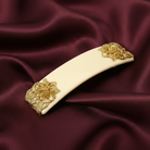Decorative hair clip with gold floral designs on a maroon fabric background.