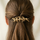 Gold hair accessory with horse design in a person's hair against a neutral background