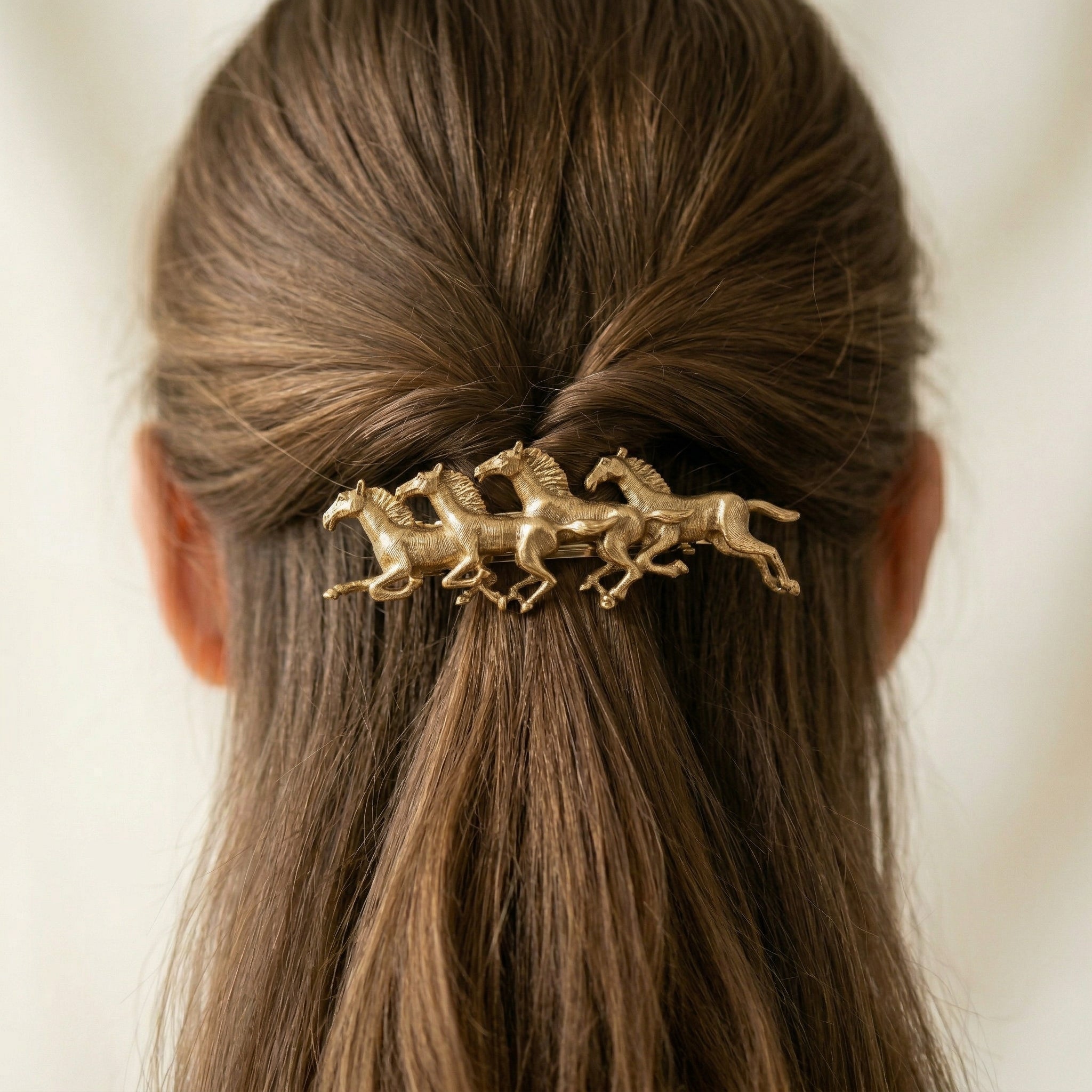 Gold hair accessory with horse design in a person's hair against a neutral background