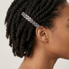 Person with braided hair wearing a decorative hair barrette with several crystals on a plain background