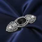 Decorative brooch with a black gemstone and faux pearls on a dark blue satin background.