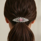 Hair barrette with a pink gemstone and lace design on a person's hair.