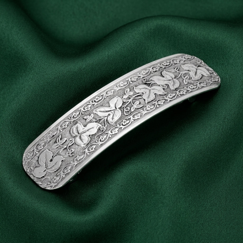 Silver floral design barrette resting on dark green fabric