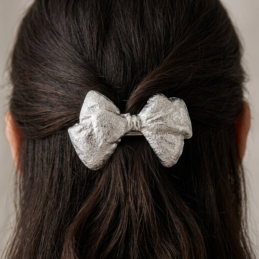 Silver bow hair barrette on dark hair against a neutral background