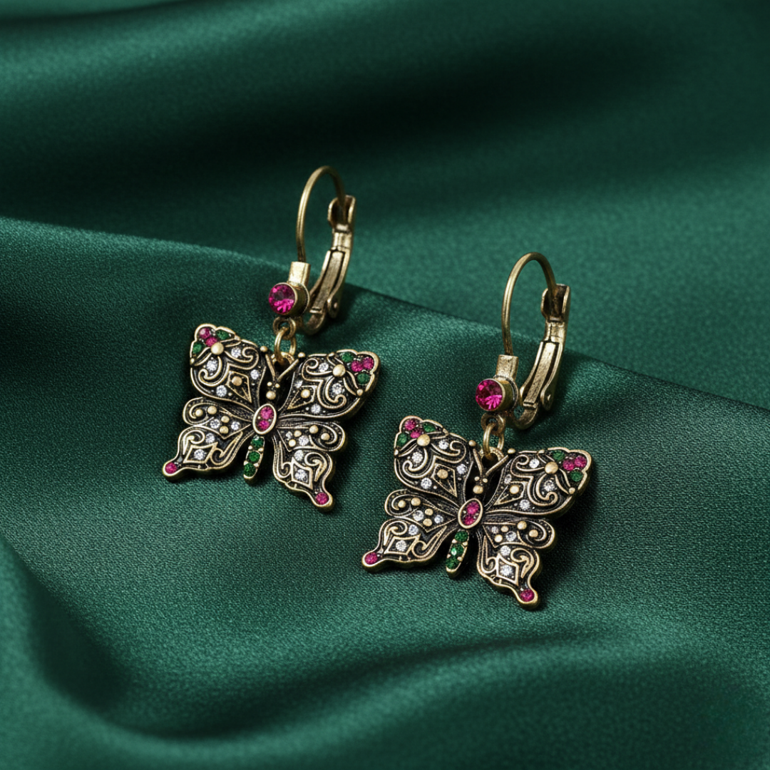 Gold butterfly-shaped earrings with crystals a green fabric background