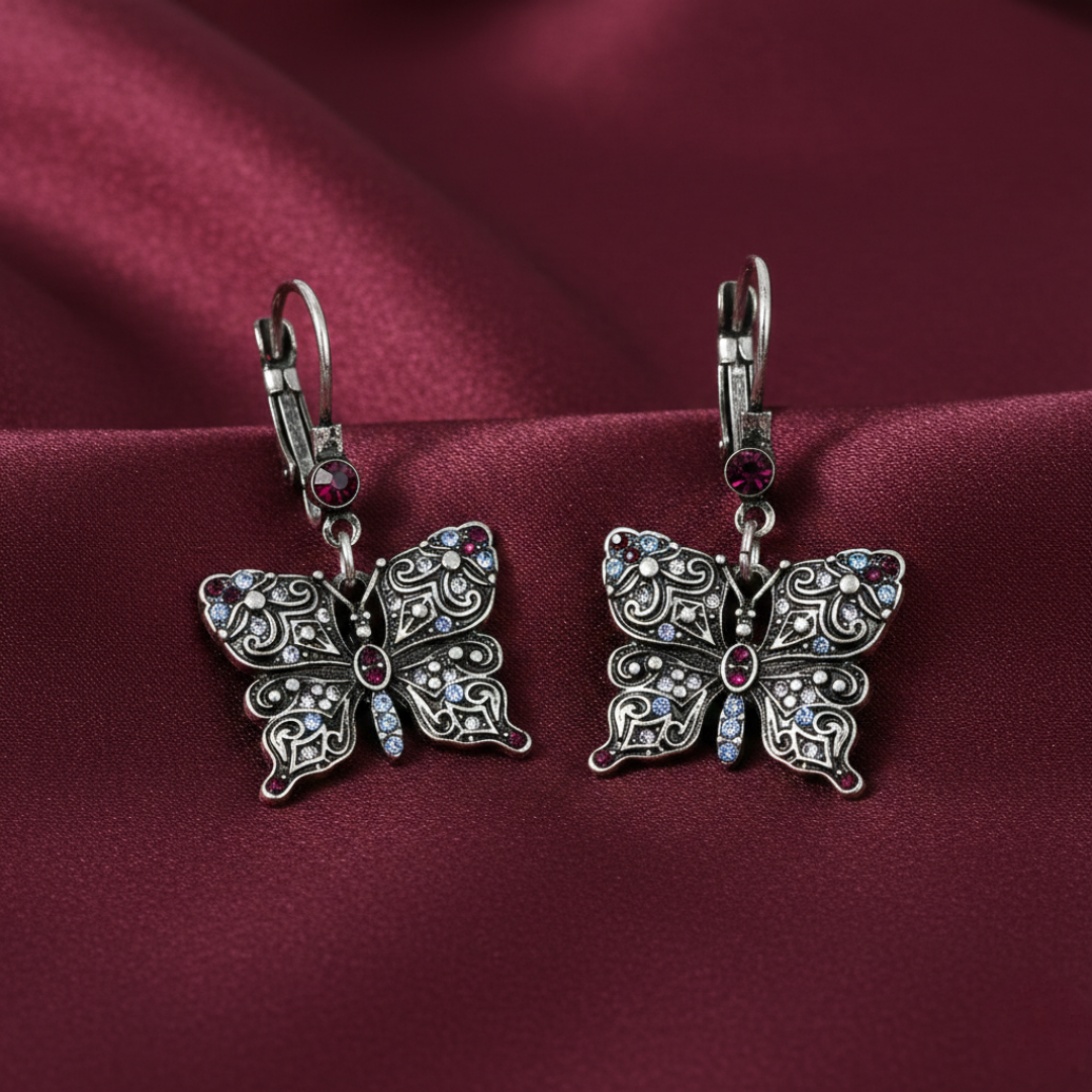 Silver butterfly-shaped earrings with crystals on a burgundy fabric background