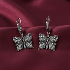 Silver butterfly-shaped earrings with crystals on a burgundy fabric background