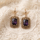 Brontë Filigree Octagon Amethyst Crystal Drop Earrings resting on white laced fabric