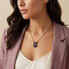 Woman wearing a necklace with a purple pendant against a beige background