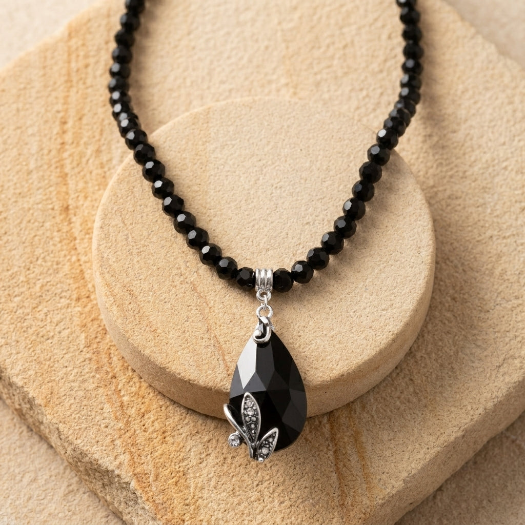 Regal Jet Black Teardrop Crystal Pendant Glass Bead Strand Necklace on light sandstone surface