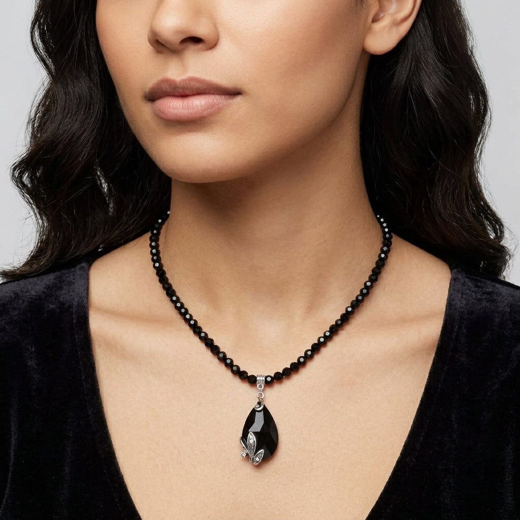 Woman wearing a black dress with a black beaded necklace with a teardrop pendant on a plain background