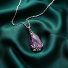 Purple teardrop pendant necklace on a green satin background