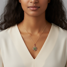 Woman wearing a gold necklace with gemstones and crystal on the pendant against a neutral background