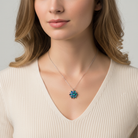 Woman wearing a necklace with a blue floral pendant against a neutral background